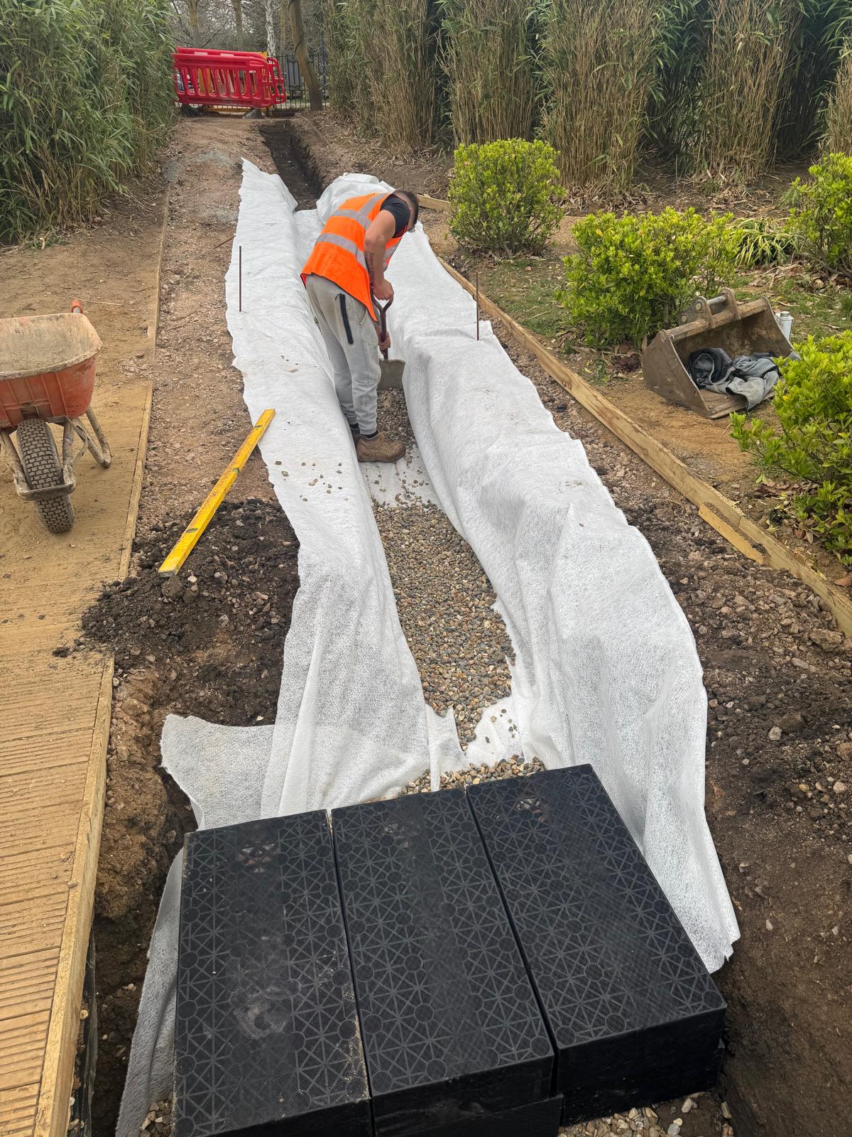 Worker spreading gravel over fabric-lined soakaway trench